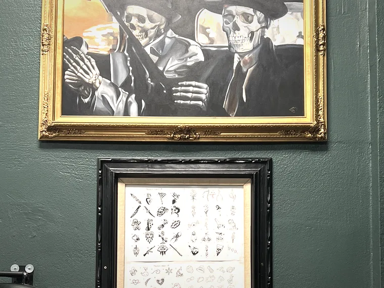 A gold-framed painting of two skeletons in suits, above a framed flash sheet